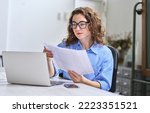 Young busy business woman manager, lawyer or company employee holding accounting bookkeeping documents checking financial data or marketing report working in office with laptop. Paperwork management