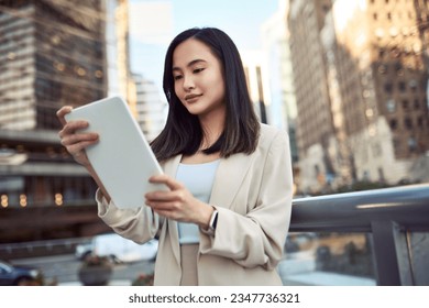 Young busy pretty Asian business woman professional office manager executive or global international company employee standing on big city street outside using digital tablet fintech pad device. - Powered by Shutterstock