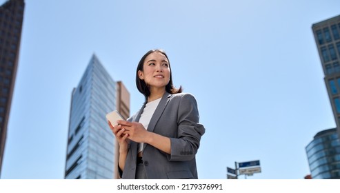Young busy successful beautiful Asian business woman  korean professional businesswoman holding cellphone using smartphone standing walking big city urban street outside 