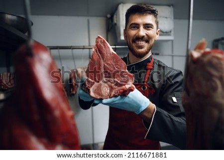 Young butcher holding raw meat steaks in fridge of grocery shop Stock foto © 