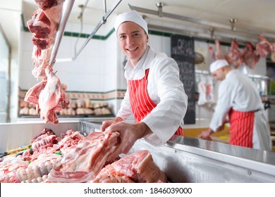 A young butcher smiling and holding meat near the camera in a meat shop.