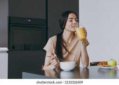 Young Calm Brunette Housewife Happy Woman 20s Wearing Casual Clothes Beige Shirt Eat Oatmeal Porridge Muesli Drink Juice Cooking Food In Light Kitchen At Home Alone. Healthy Diet Lifestyle Concept.