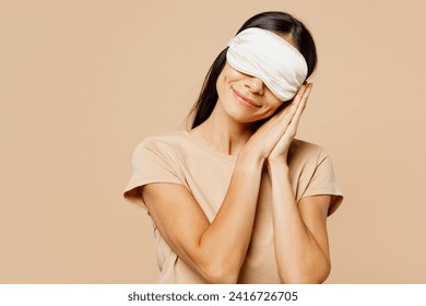 Young calm Latin woman wear pyjamas jam sleep eye mask rest relax at home cover eyes hold folded hands under cheek isolated on plain pastel light beige background studio. Good mood night nap concept - Powered by Shutterstock