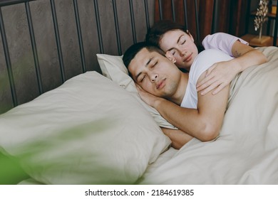 Young Calm Tranquil Lovely Couple Two Family Man Woman She He Wearing T-shirt Pajama Hugging Cuddle Sleep Lying In Bed Rest Spend Time Together In Bedroom Home In Own Room Hotel. Real Estate Concept