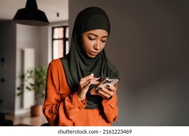 Young calm woman in hijab scrolling her phone at home - Powered by Shutterstock