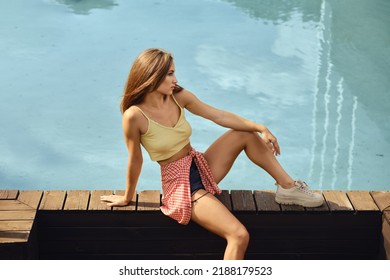 Young Calm Woman Sits On Wooden Flooring In Public Pool