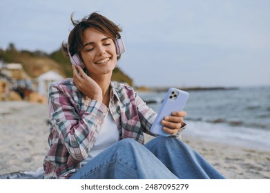 Young calm woman wear shirt casual clothes headphones sits listen music use mobile cell phone listen music rest on sea ocean sand shore beach outdoor seaside in summer day free time. Lifestyle concept - Powered by Shutterstock