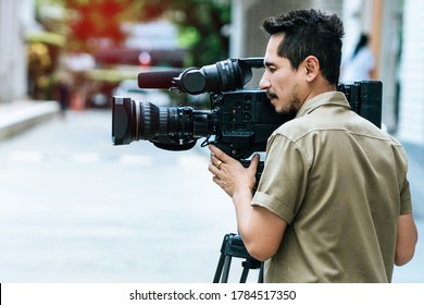 Young cameraman using a professional camcorder outdoor filming news with blur background.