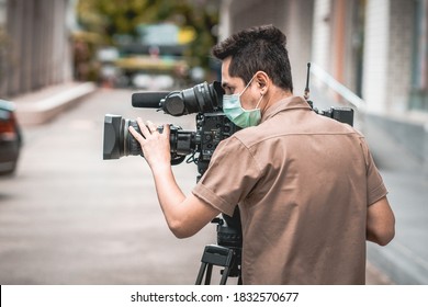 Young Cameraman Using A Professional Camcorder Outdoor Filming News While Wearing Mask Prevent Covid-19 Or Coronavirus Quarantine Pandemic.