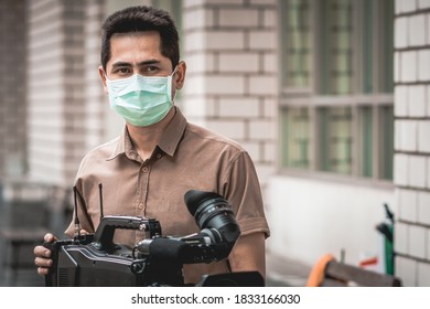 Young Cameraman Using A Professional Camcorder Outdoor Filming News While Wearing Mask Prevent Covid-19 Or Coronavirus Quarantine Pandemic.