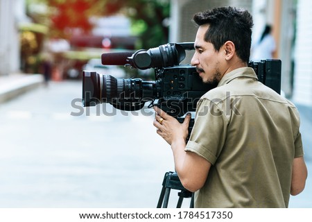 Young cameraman using a professional camcorder outdoor filming news with blur background.