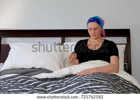 Young cancer patient in headscarf in bed looks at bottle of pills