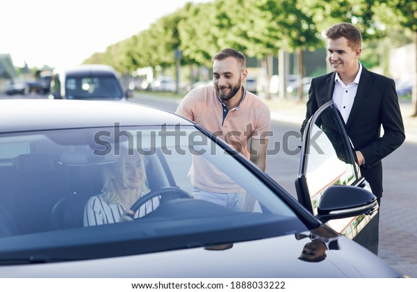 A young car\
dealer in a business suit shows buyers a new car. Young couple, man\
and woman, buy a car. Happy woman sitting behind the wheel.\
Purchase of machines, test\
drive