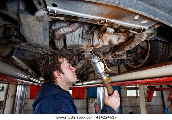 young\
car mechanic checks a car with an inspection\
lamp