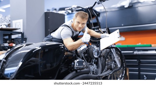 Young car mechanic is diagnosing a motorcycle and holding clipboard and thumbs up. Quality motorcycle service concept - Powered by Shutterstock