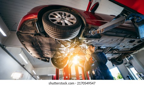 Young car mechanic at repair service station inspecting car wheel and suspension detail of lifted automobile. Bottom view. - Powered by Shutterstock