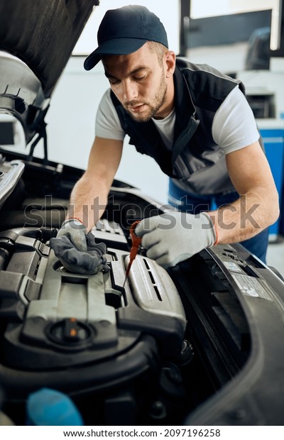 Young car repairman checking oil level during\
engine maintenance in a\
workshop.