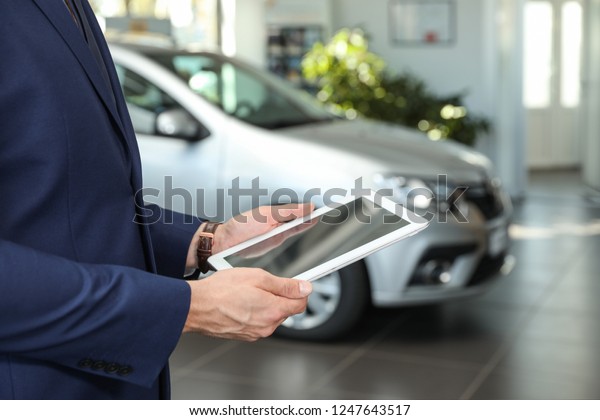 Young car\
salesman with tablet in dealership,\
closeup