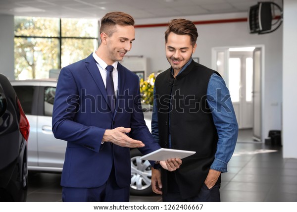 Young car\
salesman working with client in\
dealership