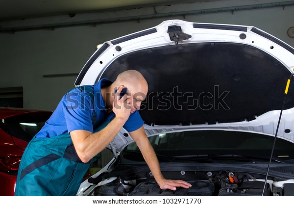 Young car service technician he´s calling while\
repair the car engine\
motor.