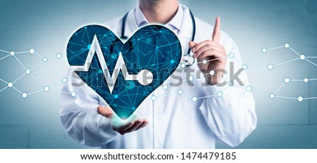 Young cardiologist holding a virtual heart displaying a pulse trace in the open palm of his right hand, while advising with raised index finger. Healthcare concept for cardiovascular health and AI.
