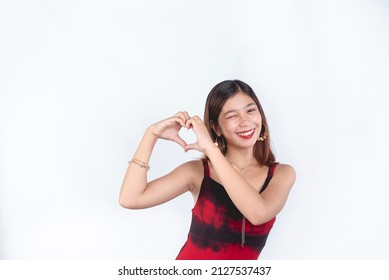 A young carefree asian woman winking and making a heart expression with both hands. Expressing love and happiness in life. Isolated on a white background. - Shutterstock ID 2127537437