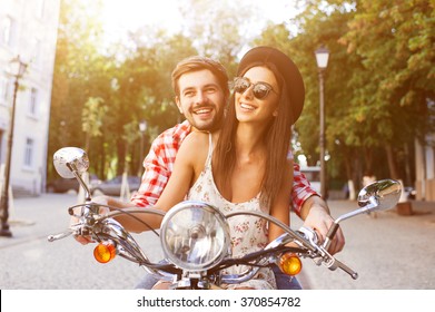 Young And Carefree Couple Learning To Drive A Scooter On A Road. Young Man Is Teaching Hipster Girl To Ride A Motorcycle.