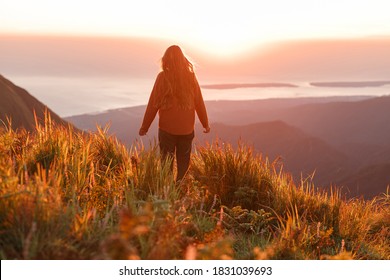 Young carefree woman dressed casual enjoying  desert landscape standing on the mountain top and look sunrise
