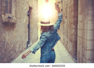 Young Carefree Woman In Hat Dancing At Old Narrow Mediterranean Street In Sunset