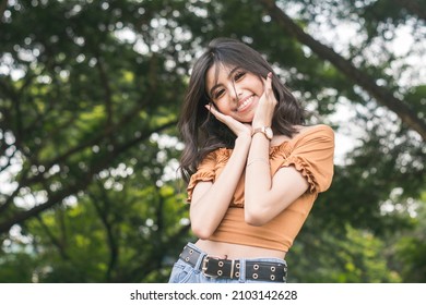 A young and carefree woman posing in a cute fashion,with hands framed on her cheeks. - Shutterstock ID 2103142628