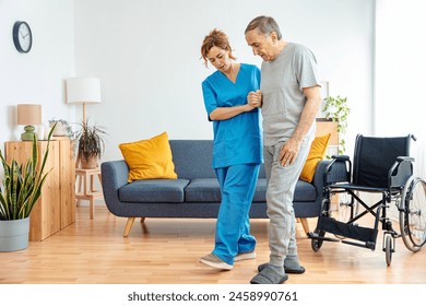 Young caregiver assisting senior man in wheelchair walking indoors - Home health care service and physiotherapy concept - Powered by Shutterstock