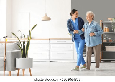 Young caregiver helping senior woman to walk in kitchen - Powered by Shutterstock