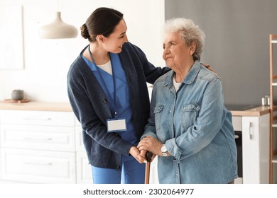 Young caregiver helping senior woman with walking stick in kitchen - Powered by Shutterstock