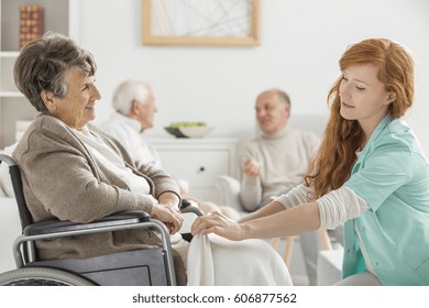 Young Caregiver Taking Care Of Older Disabled Woman In Nursing Home