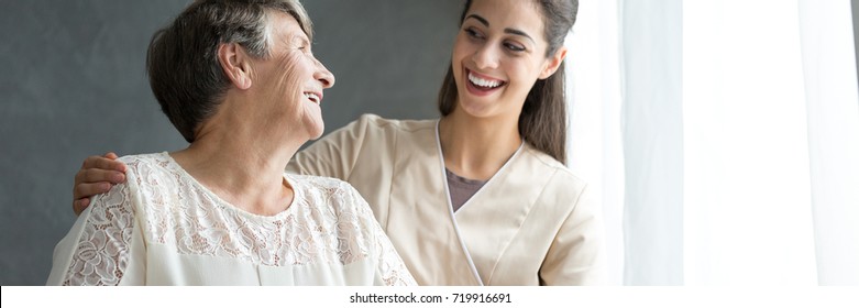 Young caregiver in uniform hugging smiling elderly woman during a home visit