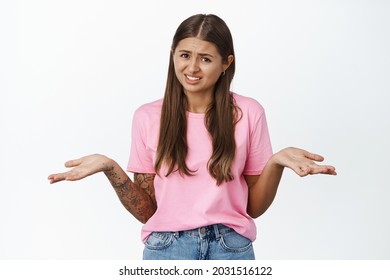 Young Careless Glamour Woman Shrugging Shoulders, Spread Empty Hands Sideways And Looking Annoyed With Question, Why Bother Face Expression, White Background