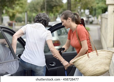 Young Carer Helping Senior Woman Getting In Car