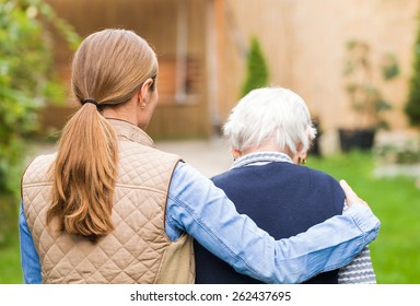 Junge Betreuerin, die mit der älteren Frau im Park spaziert