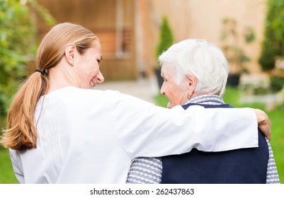 Junge Betreuerin, die mit der älteren Frau im Park spaziert