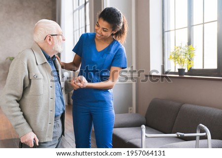 Young caring african nurse helping senior old elderly man grandfather walk . Disable old man trying to walk with the assistance aid of female doctor.
