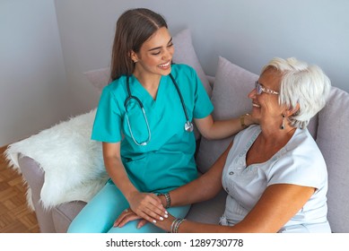 Young Caring Lovely Caregiver And Happy Ward. Image Of Caregiver And Senior Resting In The Living Room. Smiling Caregiver Taking Care Of A Happy Elderly Woman