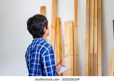Young carpenter checking woodwork stock at factory storage. Man counting timber beams wood inventory in carpentry workshop