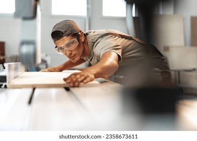 Young carpenter cutting a piece of wood in using a circular saw in furniture factory - Shutterstock ID 2358673611