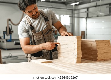 Young carpenter man looking and choosing wood plank at workshop in carpenter wood factory - Powered by Shutterstock