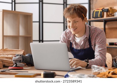 Young carpenter using laptop at table in workshop