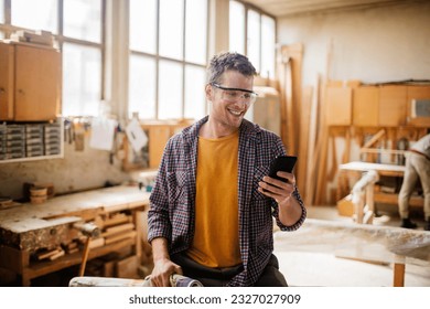 Young carpenter using a smart phone while working in his woodworking workshop - Powered by Shutterstock