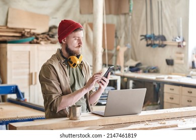Young Carpenter Using Smartphone In Workshop