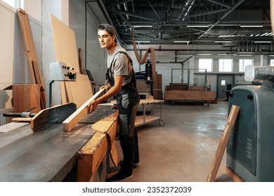 Young carpenter working on woodworking machines in the furniture factory