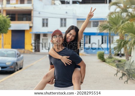 Young an carrying young woman on her back piggyback smiling. Woman making peace and love hand sign gesture