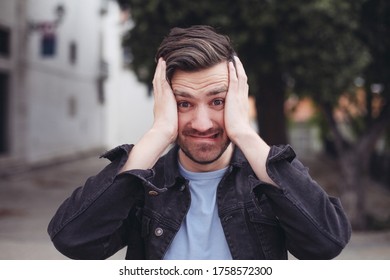 Young casual man holds his head with hands, looks scared and shocked. Concepts of getting unexpected news. Outside, outdoors, man in a park